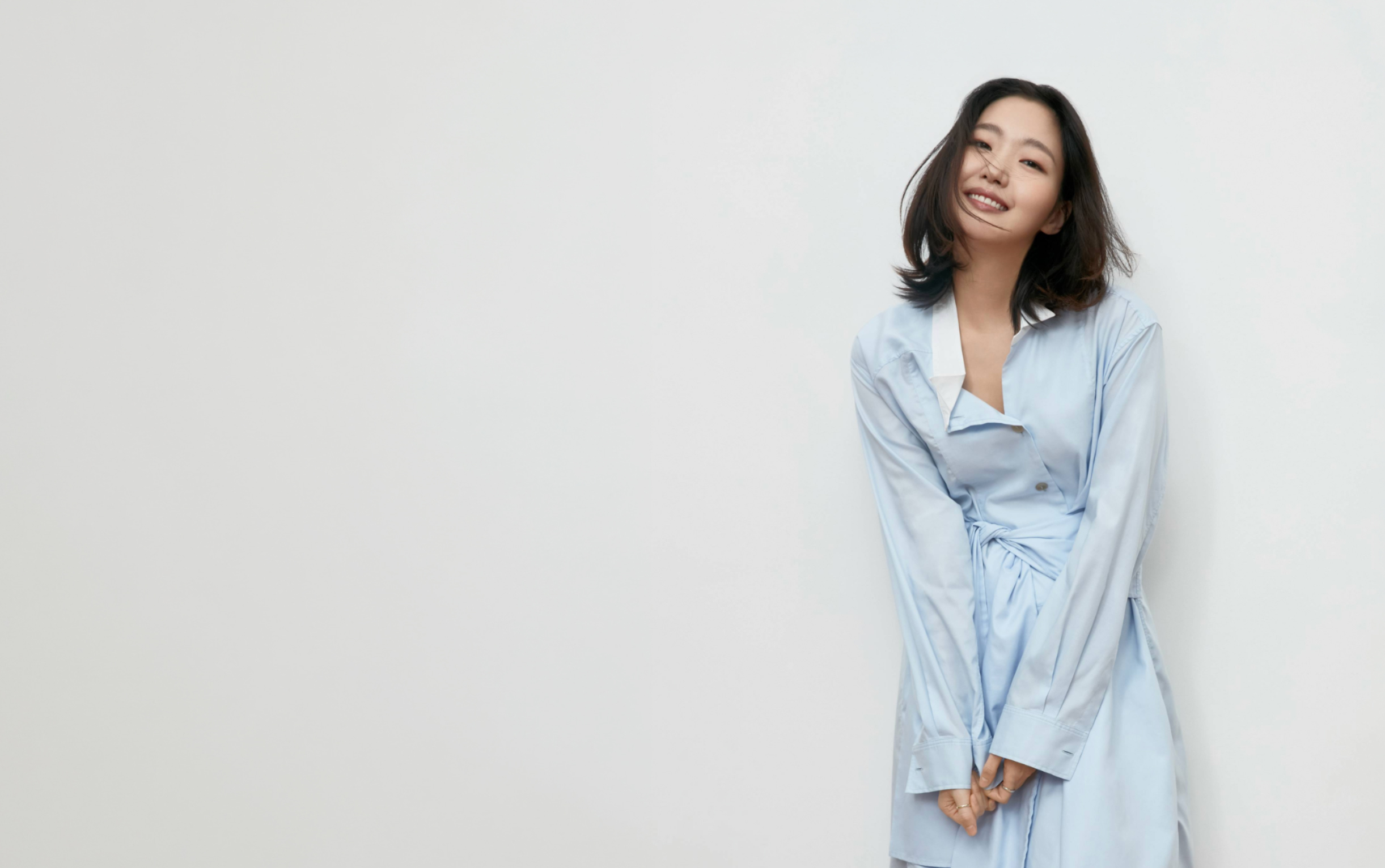 밝은 회색 배경 앞에서 연한 하늘색 셔츠 드레스를 입고 미소 짓는 배우 김고은